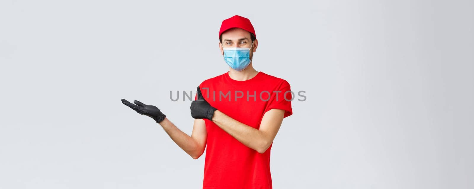 Groceries and packages delivery, covid-19, quarantine and shopping concept. Satisfied smiling courier in red uniform, face mask and gloves, holding promo banner in hand and thumb-up, recommend by Benzoix