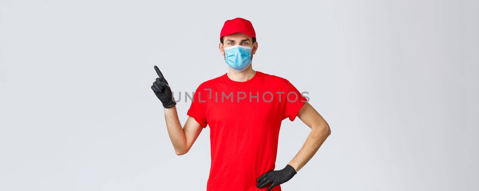 Covid-19, self-quarantine, online shopping and shipping concept. Delivery man in red cap and t-shirt, medical mask with gloves to protect clients and employees, pointing finger left at promo, show ad by Benzoix