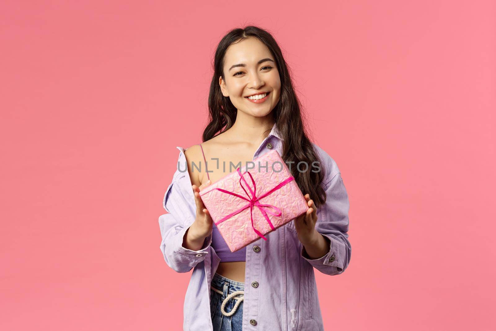 Girl have a present for you. Portrait of stylish pretty young asian female holding wrapped gift box and smiling at camera as being invited to birthday party, standing pink background.