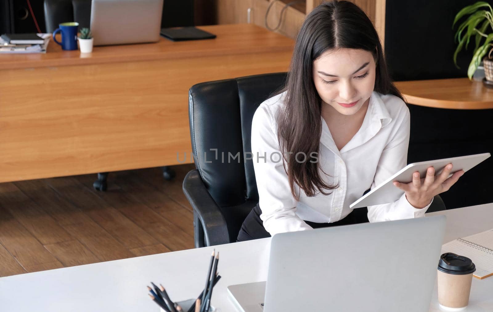 Young asian businesswoman works on tablet with laptop at the office..