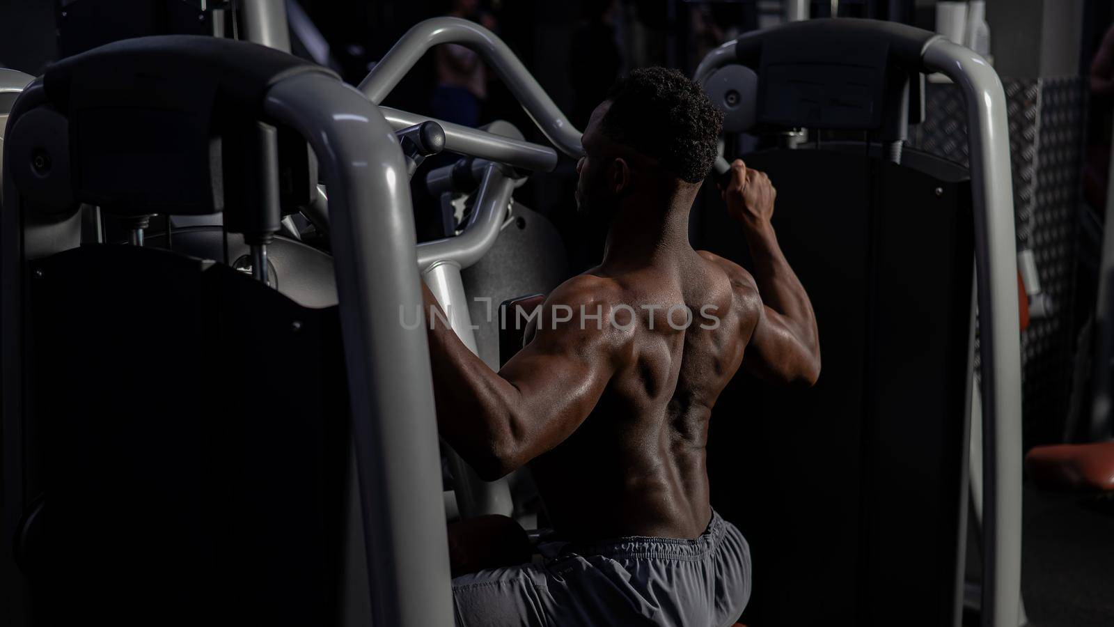 Shirtless african american man doing back exercises on a machine in the gym