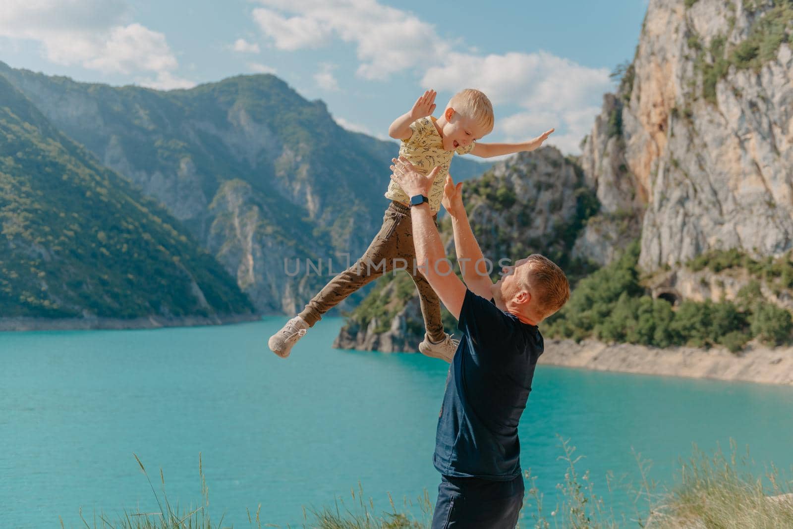 Summertime! Happy joyful child, father fun throws up son in the air, carefree, blue sky, family, travel, vacation, childhood, father's day - concept. Sunlight on the sunset. Father picking up smiling toddler outdoor by Andrii_Ko