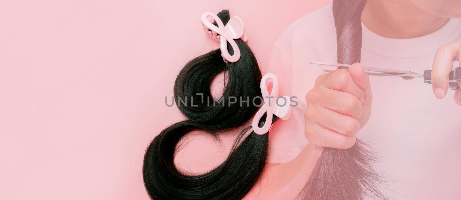 Hair donation for breast cancer person concept. Donate hair to wigs for breast cancer patients. Donate to cancer charity. Asian woman cutting long hair with scissors for donating on pink background.