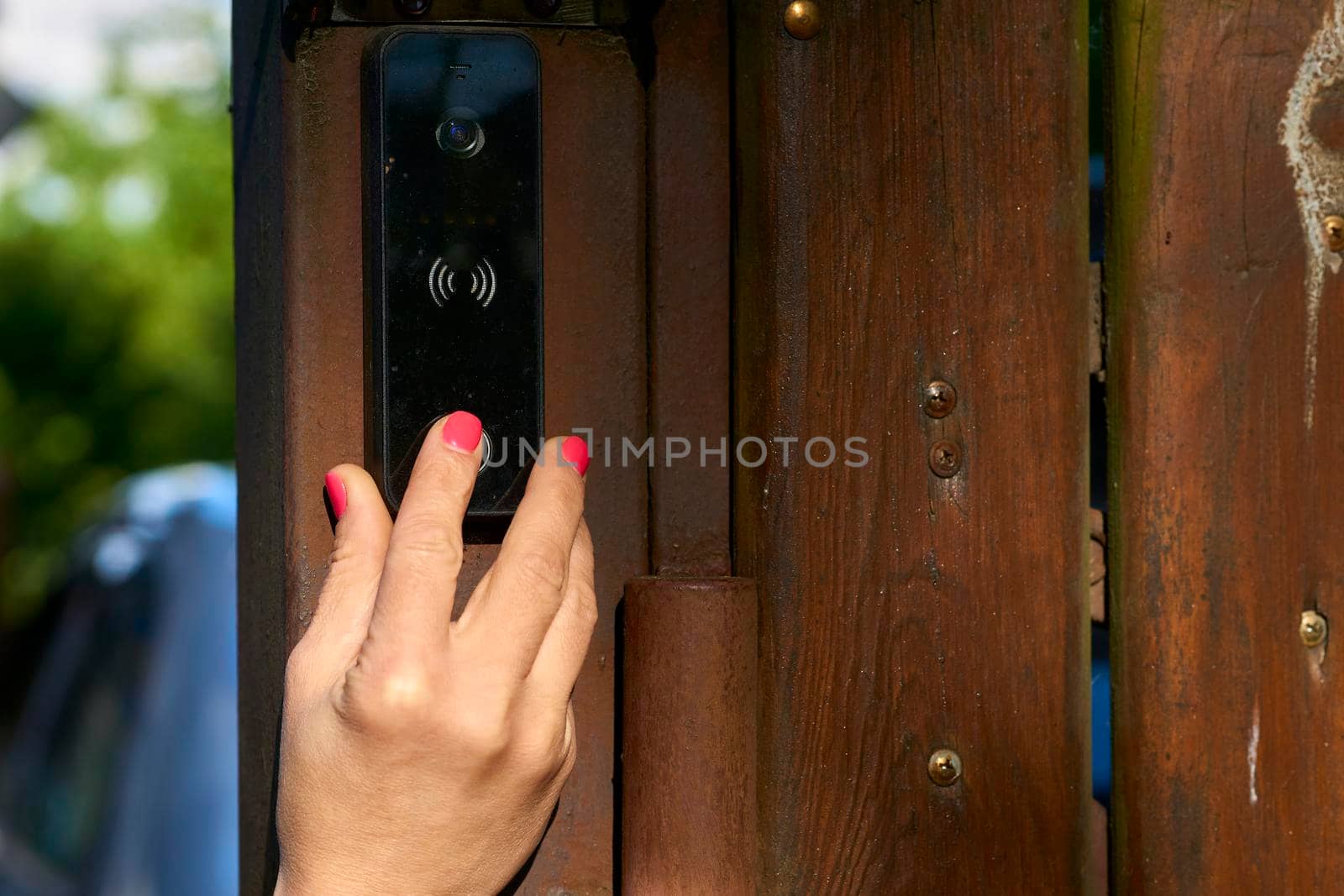 a bell in a building which can be rung by visitors outside to signal their arrival. Woman's hand pressing a doorbell on a wooden fence in the garden. High quality photo