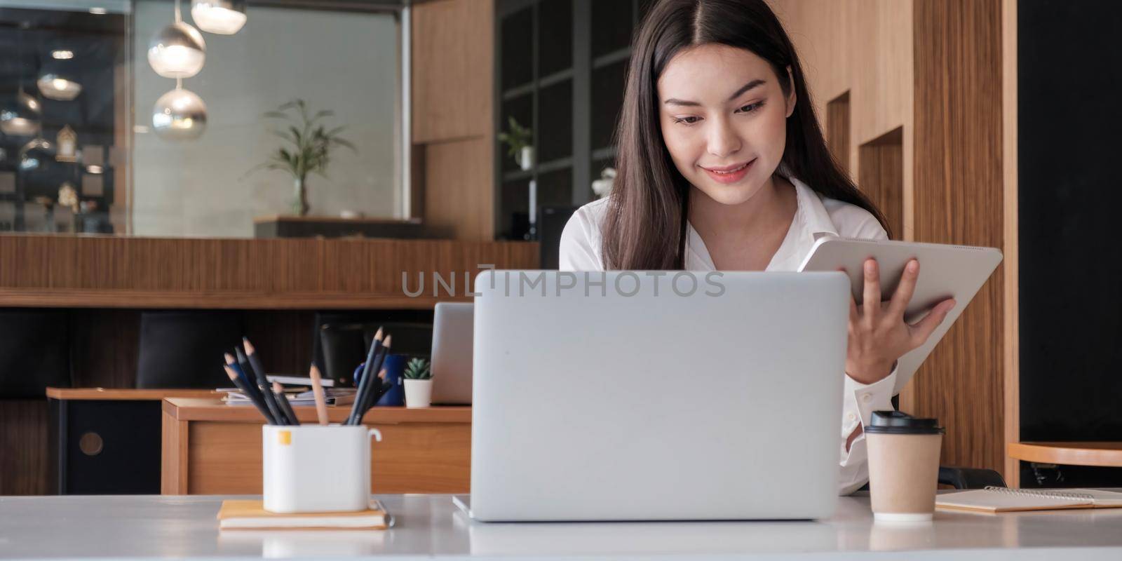 Young asian businesswoman works on tablet with laptop at the office..