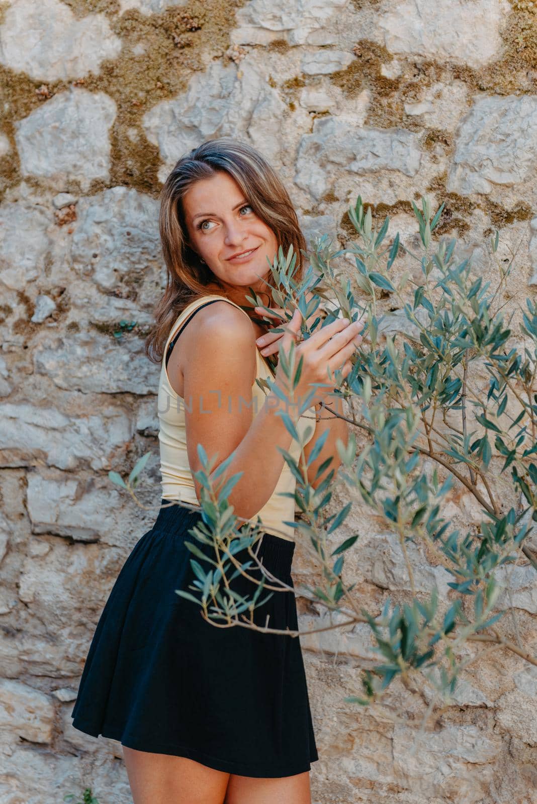 Girl tourist walking through ancient narrow street on a beautiful summer day in MEDITERRANEAN MEDIEVAL CITY , OLD TOWN bUDVA, MONTENEGRO. Young beautiful cheerful woman walking on old street at tropical town. Pretty girl looking at you and smiling