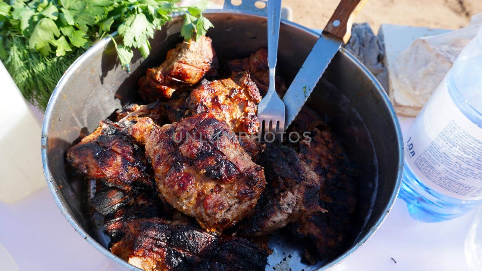 Ready-made delicious meat covered with a hot delicious crust in a cup. Nearby there are greens, a fork and a knife. The golden crust is slightly burnt on the grill. Food in nature