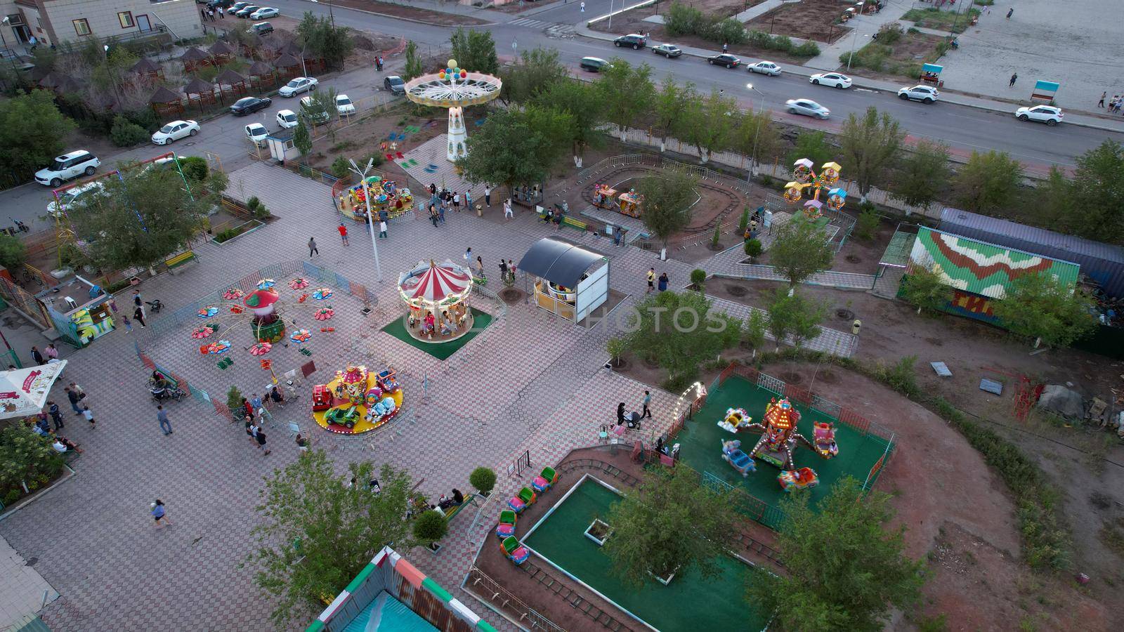 A bird's-eye view of children's attractions from a drone. Bright lights from different lanterns. Carousels are spinning. People are resting. The attractions are located on the shore of Lake Balkhash