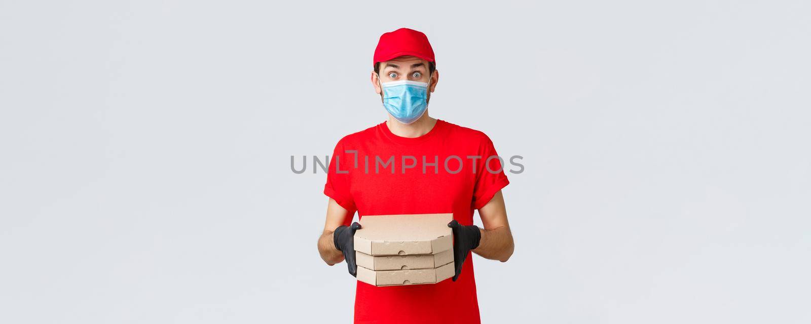 Food delivery, application, online grocery, contactless shopping and covid-19 concept. Surprised courier in red uniform, face mask and gloves, look imressed, bring clients pizza, hold boxes.