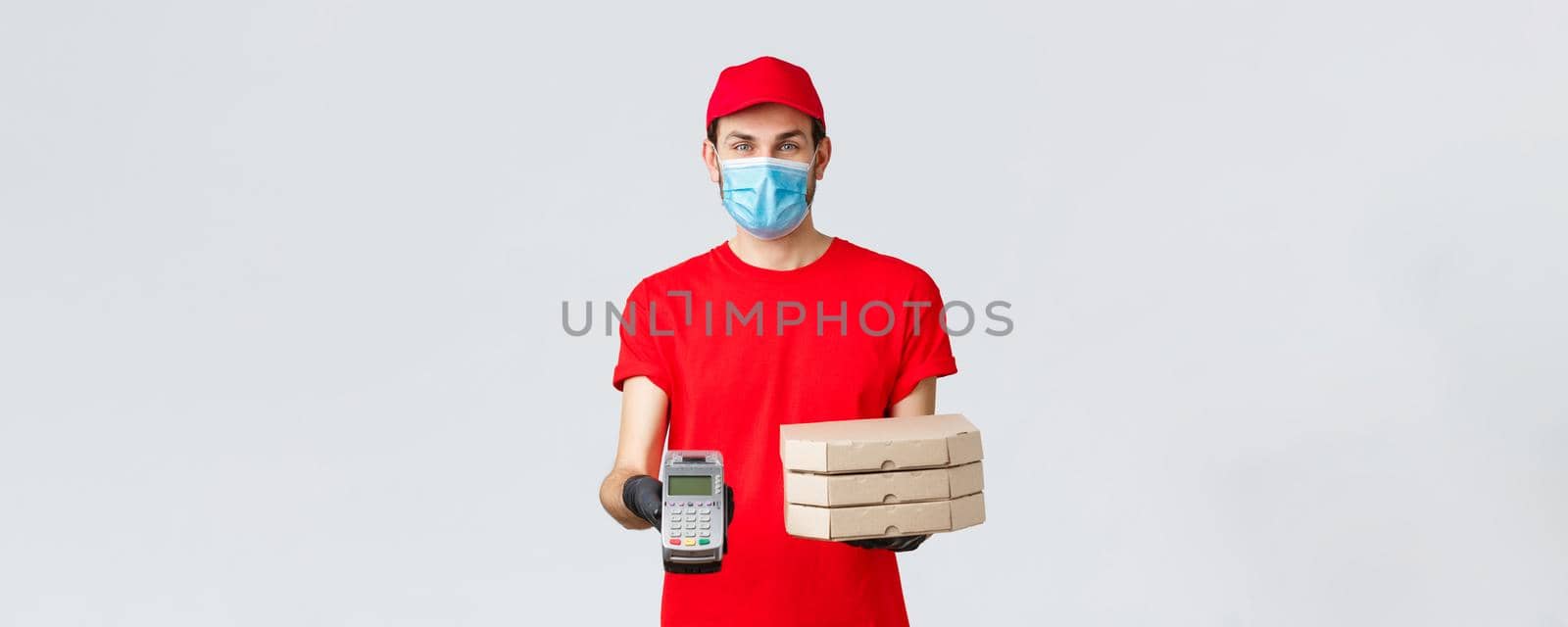 Food delivery, application, online grocery, contactless shopping and covid-19 concept. Friendly courier in red uniform, face mask and gloves, holding order pizza boxes and give client POS terminal by Benzoix