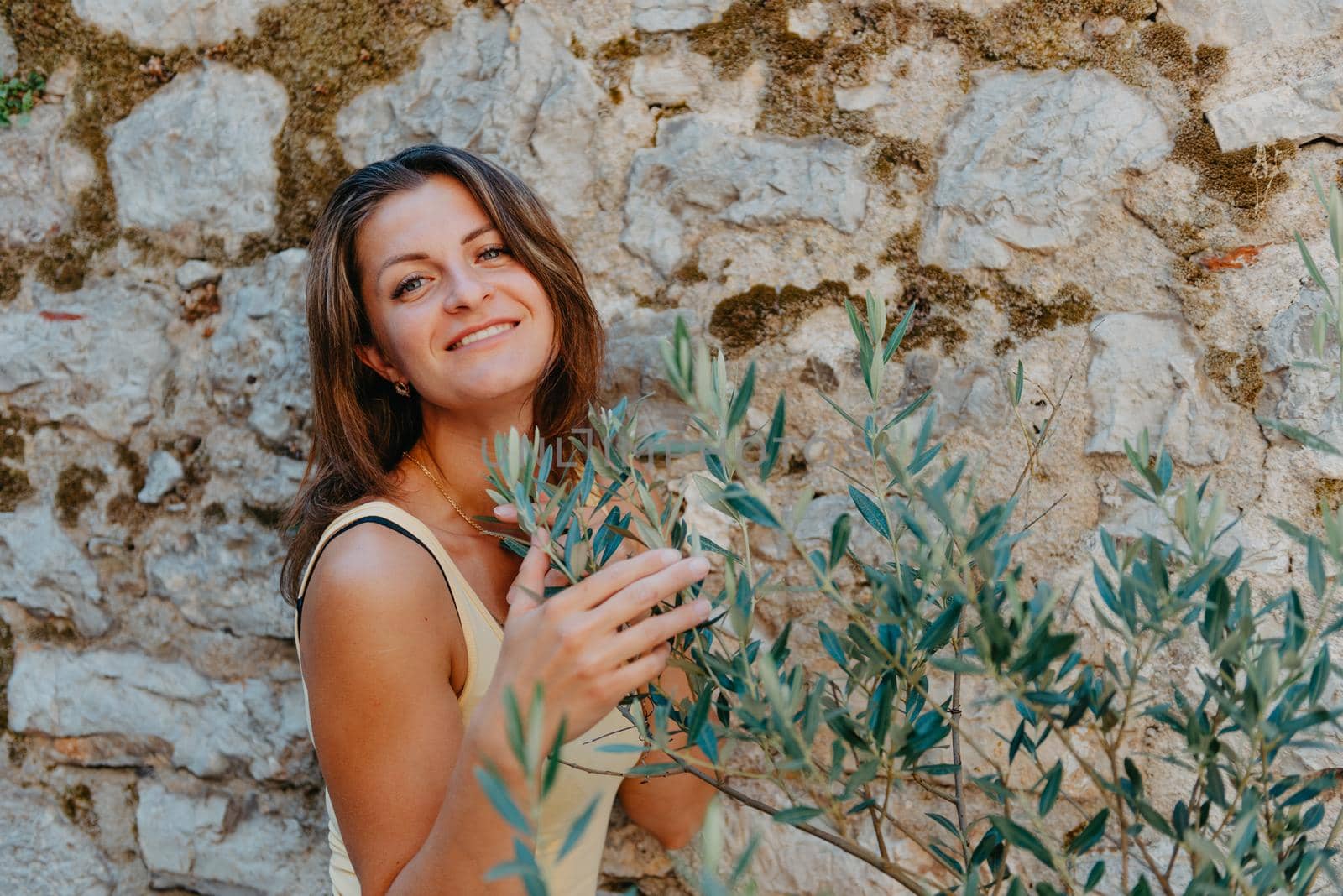 Girl tourist walking through ancient narrow street on a beautiful summer day in MEDITERRANEAN MEDIEVAL CITY , OLD TOWN bUDVA, MONTENEGRO. Young beautiful cheerful woman walking on old street at tropical town. Pretty girl looking at you and smiling