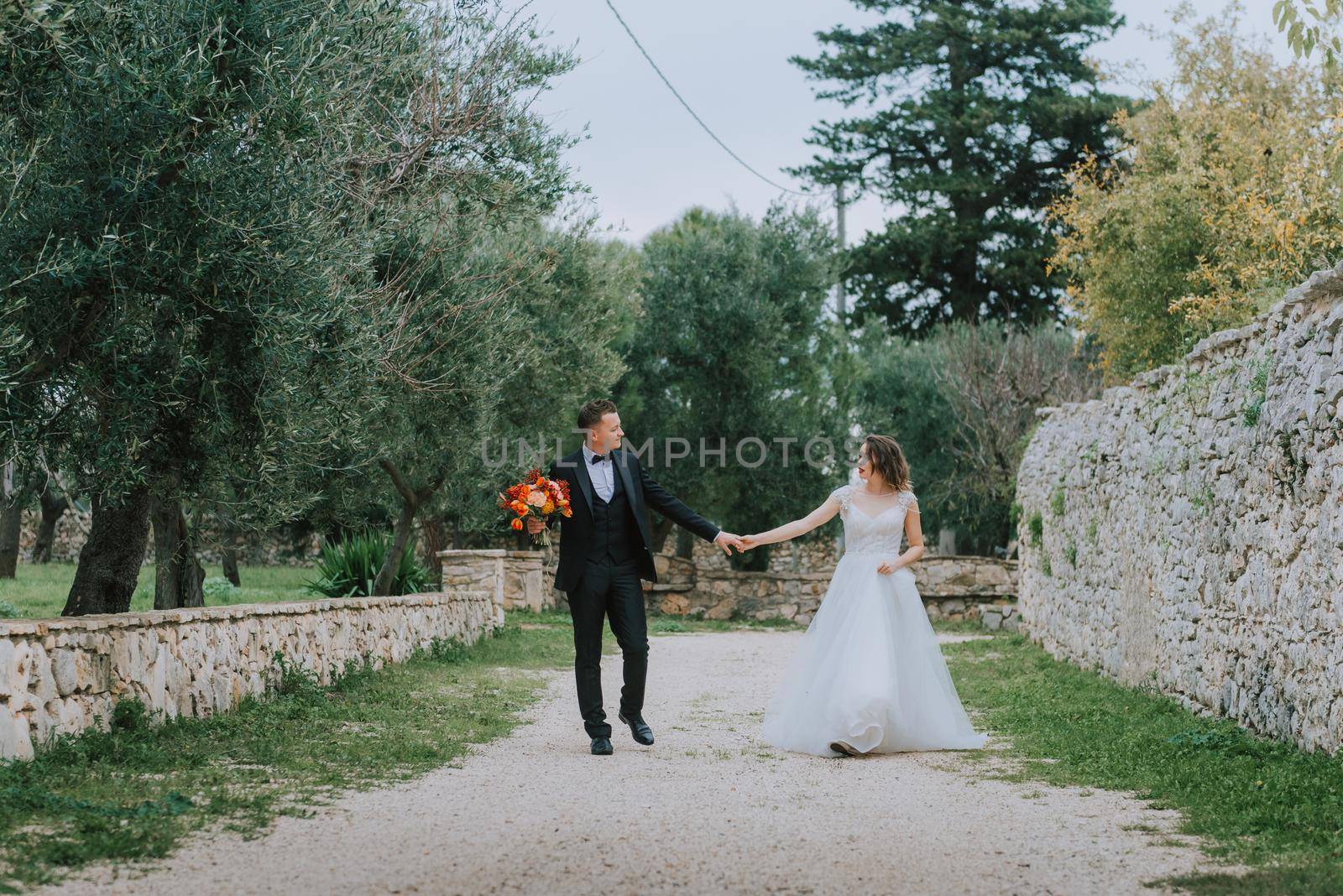 Happy stylish smiling couple walking in Tuscany, Italy on their wedding day. The bride and groom walk down the street by the hands. A stylish young couple walks. Husband and wife communicate nicely. Lovers run through the streets of the city.