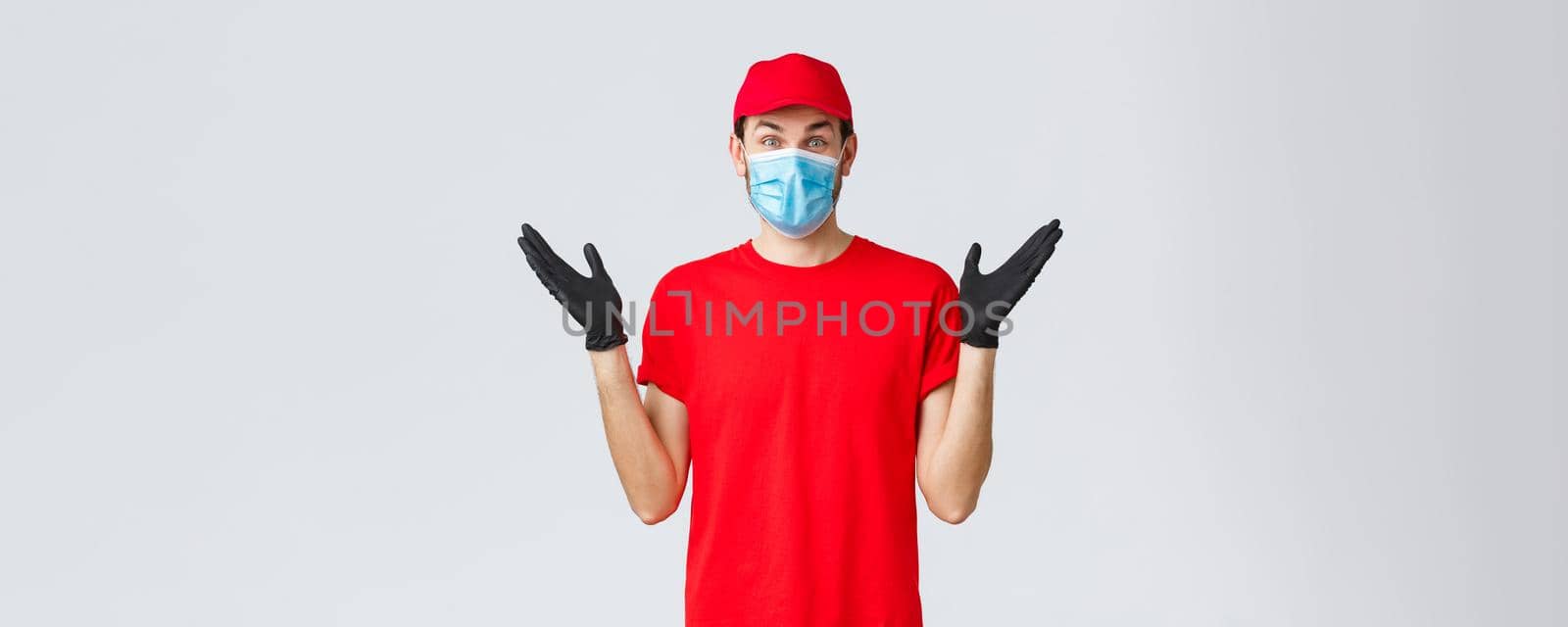 Groceries and packages delivery, covid-19, quarantine and shopping concept. Happy rejoicing delivery guy in red uniform, face mask and gloves receive good news, clap hands applause surprised.