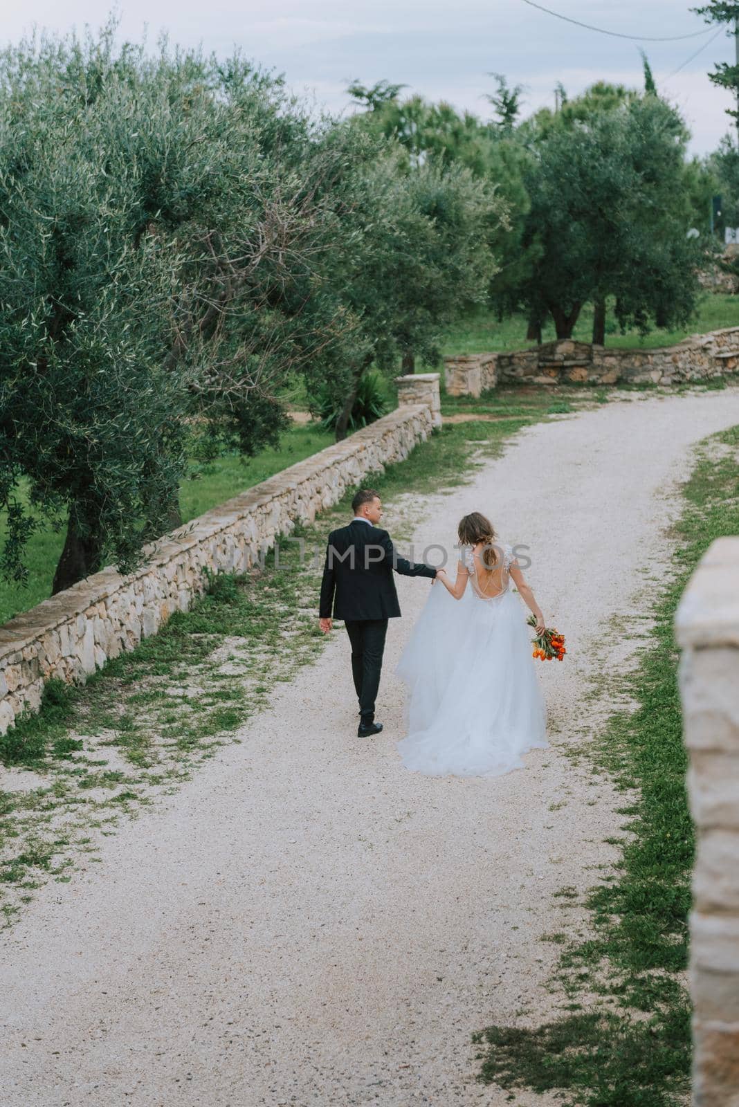 Happy stylish smiling couple walking in Tuscany, Italy on their wedding day. The bride and groom walk down the street by the hands. A stylish young couple walks. Husband and wife communicate nicely. Lovers run through the streets of the city by Andrii_Ko