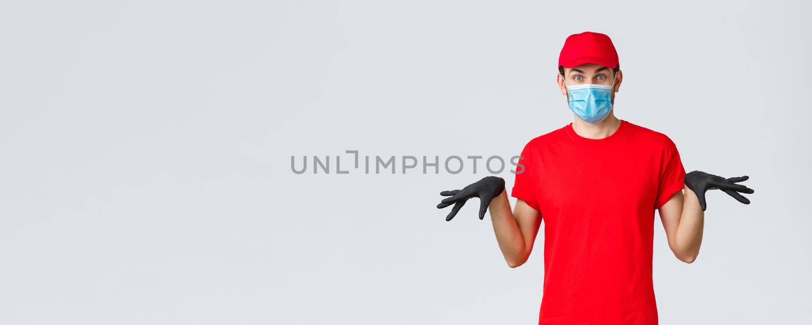 Covid-19, self-quarantine, online shopping and shipping concept. Funny courier in black rubber gloves and face mask, delivery guy in uniform gesturing reluctant, standing grey background by Benzoix