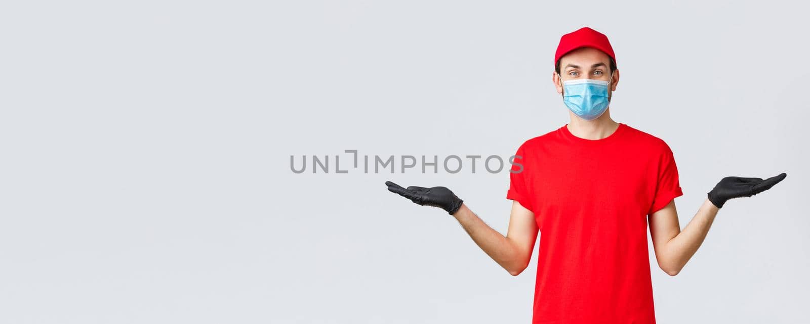 Groceries and packages delivery, covid-19, quarantine and shopping concept. Friendly delivery man in red uniform, face mask and gloves, holding two items or banners in hand, advice bonuses by Benzoix