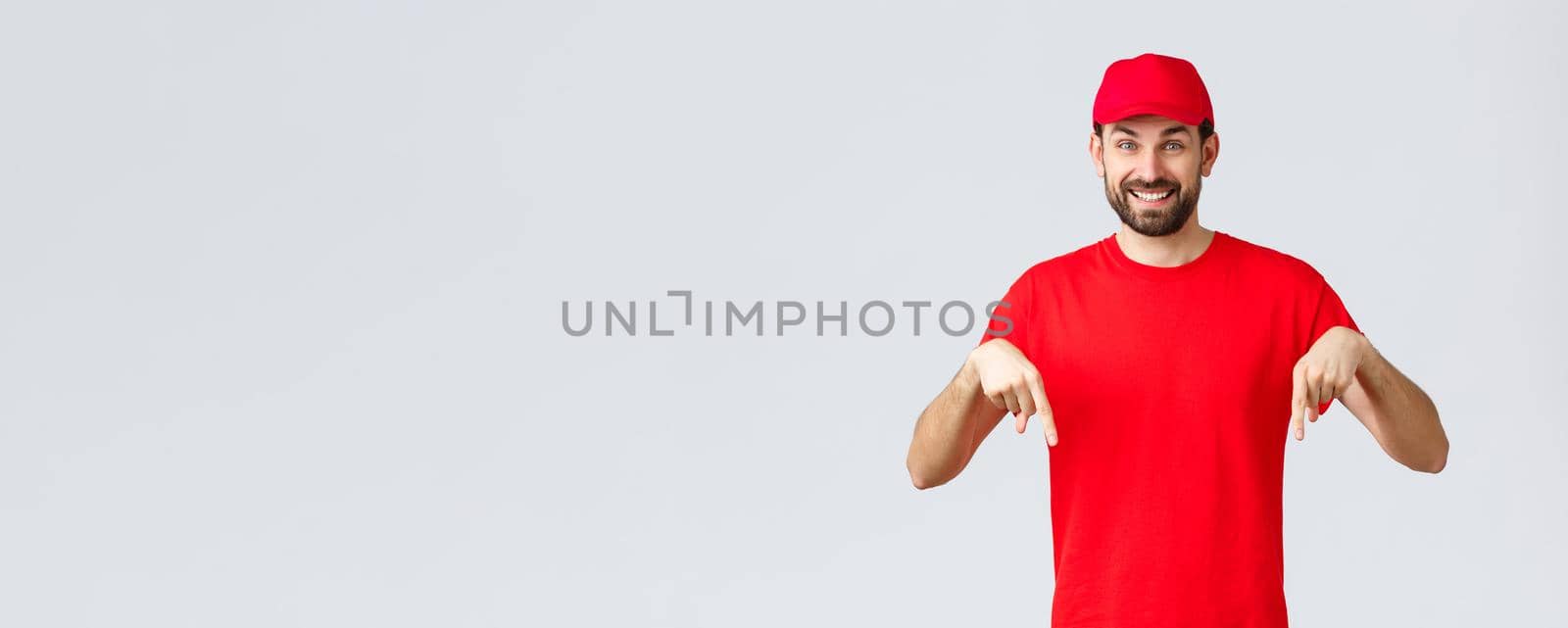 Online shopping, delivery during quarantine and takeaway concept. Cheerful friendly courier in red uniform cap and t-shirt, pointing fingers down, inform clients, recommend advertisement by Benzoix