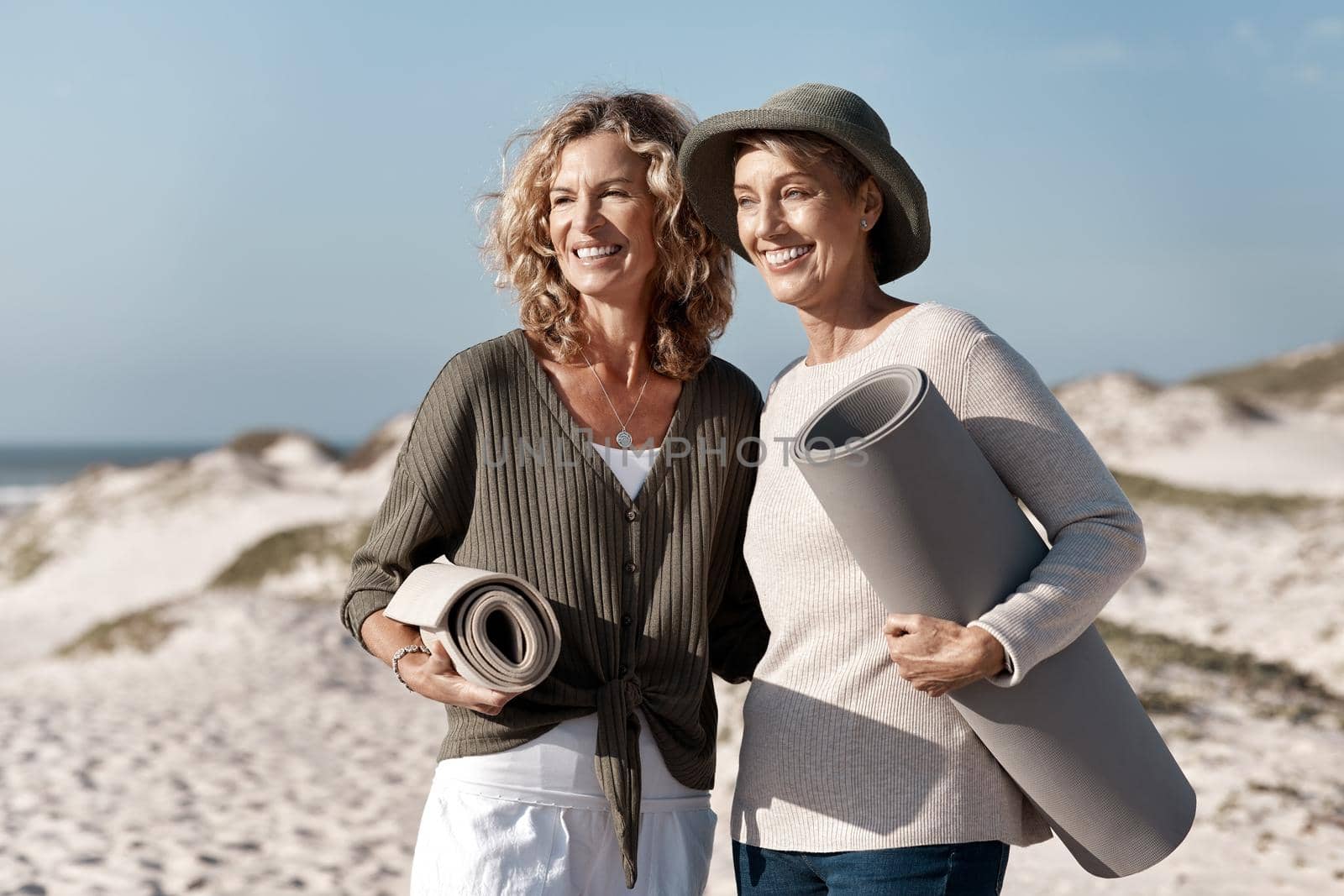 Where should we set up. two attractive mature woman standing with their on the beach. by YuriArcurs