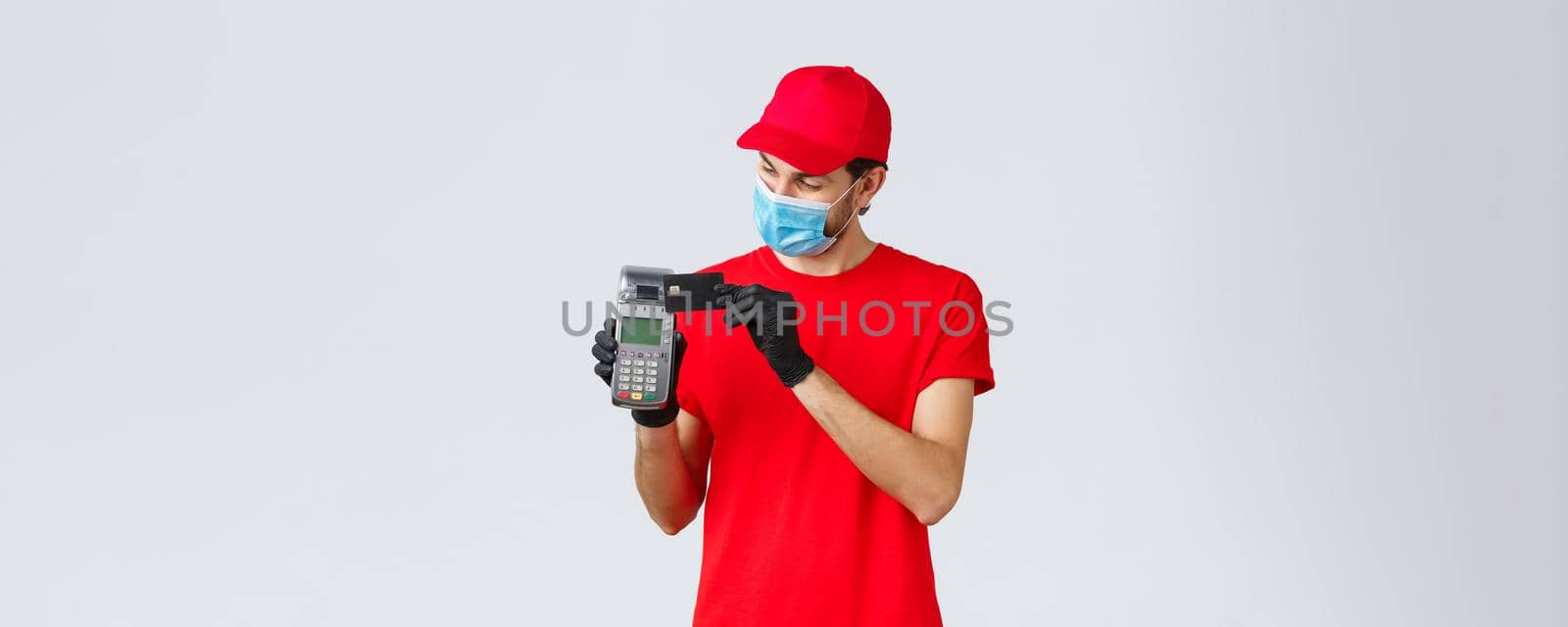 Contactless delivery, payment and online shopping during covid-19, self-quarantine. Courier in red uniform and gloves with face mask, showing POS paying terminal and credit card, pay for order by Benzoix