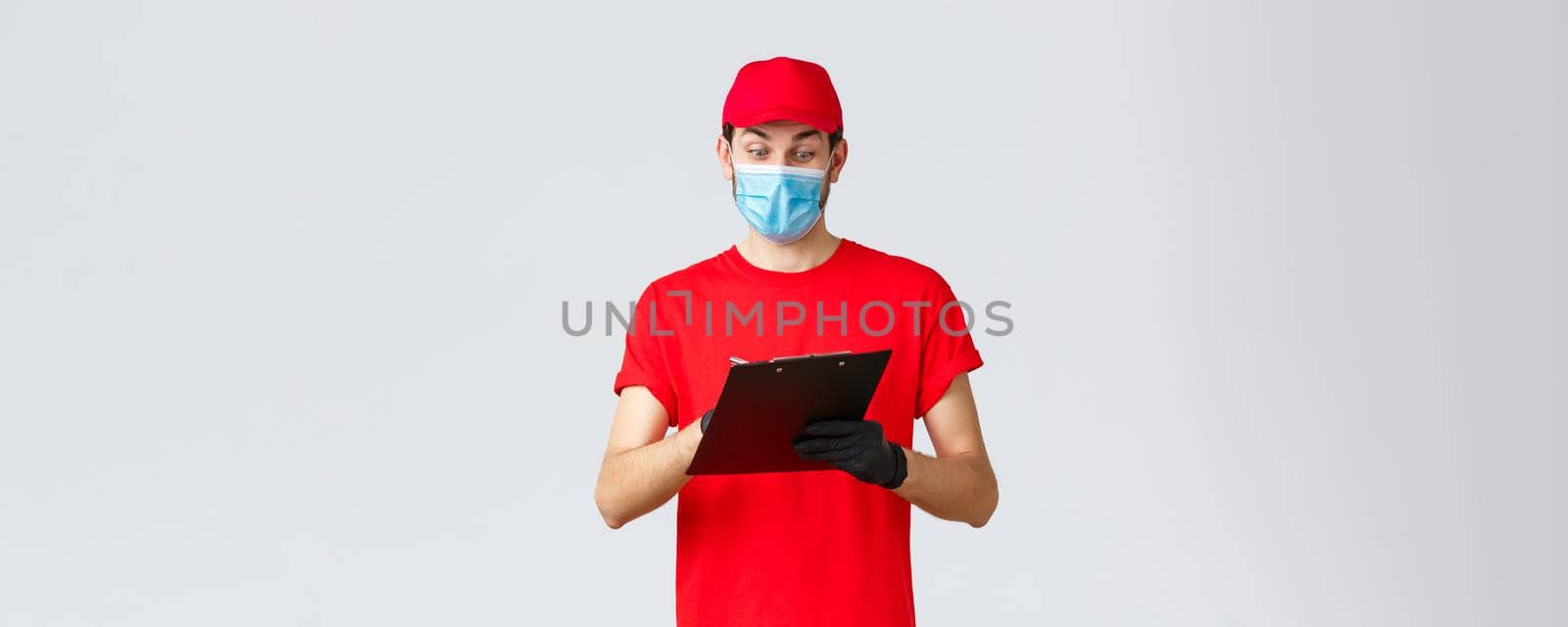 Packages and parcels delivery, covid-19 quarantine delivery, transfer orders. Enthusiastic courier in red uniform, face mask and gloves, writing down, checking order form on clipboard, deliver goods.