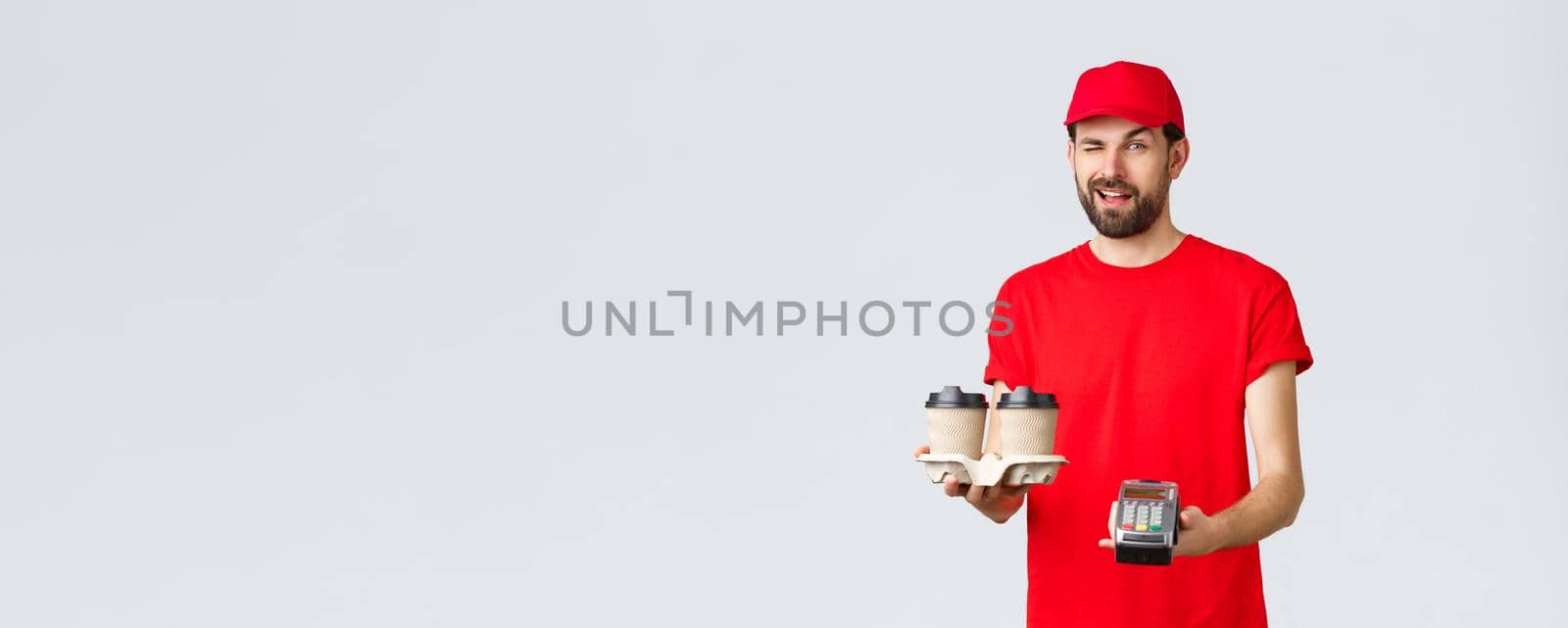 Food delivery, quarantine, stay home and order online concept. Cheeky courier in red uniform cap and t-shirt, wink to client as handing POS terminal and coffee deliver to pay contactless.