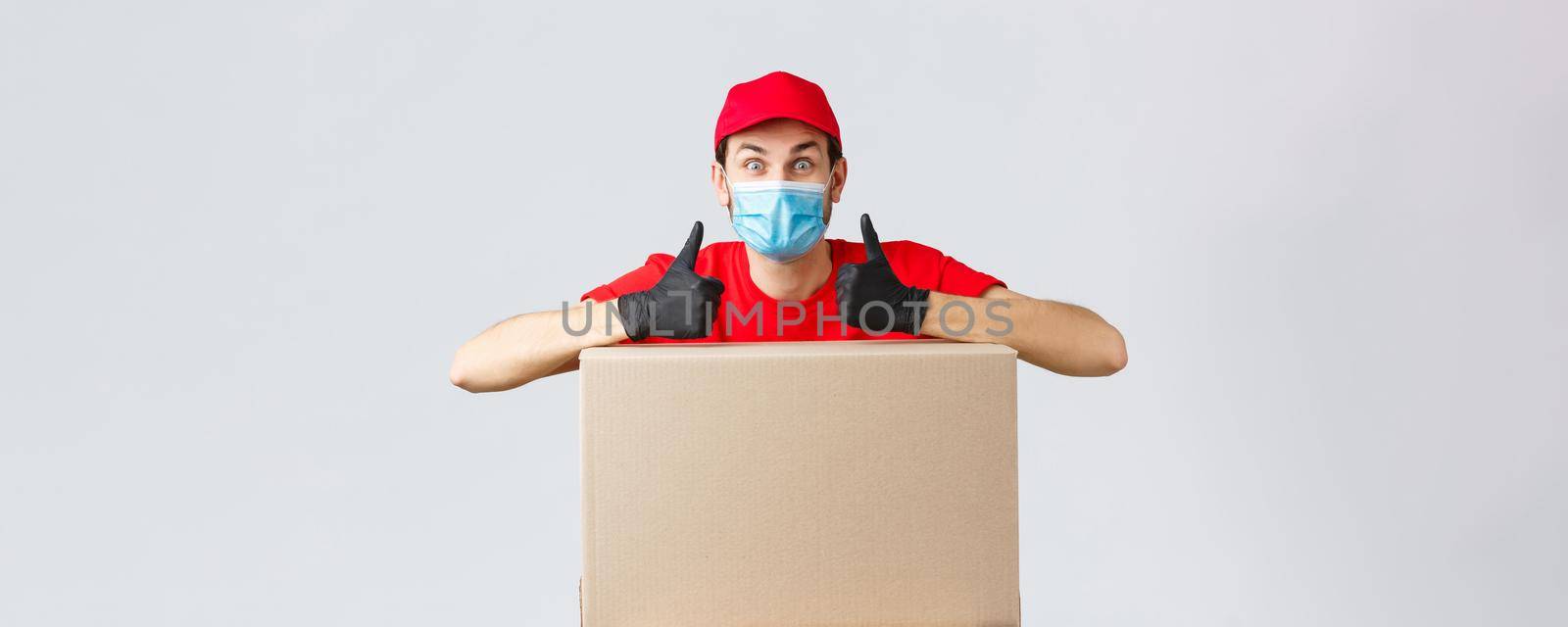 Packages and parcels delivery, covid-19 quarantine and transfer orders. Enthusiastic courier in red uniform, face mask and gloves, lean on box order and thumb-up, recommend service, express shipping.