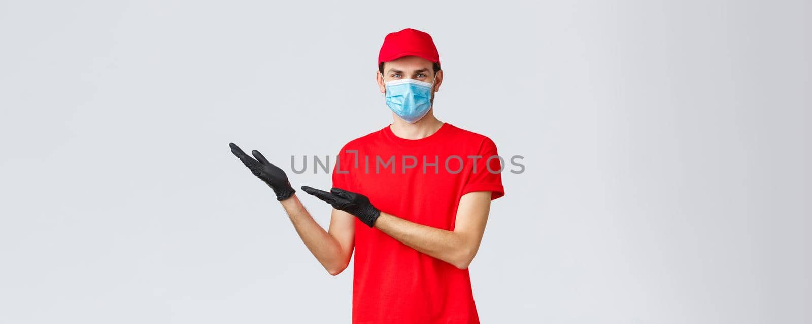 Groceries and packages delivery, covid-19, quarantine and shopping concept. Friendly delivery man in uniform, medical face mask and gloves introduce new promo, showing left banner by Benzoix