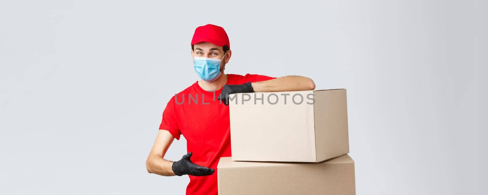 Packages and parcels delivery, covid-19 quarantine and transfer orders. Smiling courier in red uniform, gloves and medical face mask, introduce boxes to transfer your order, recommend service by Benzoix
