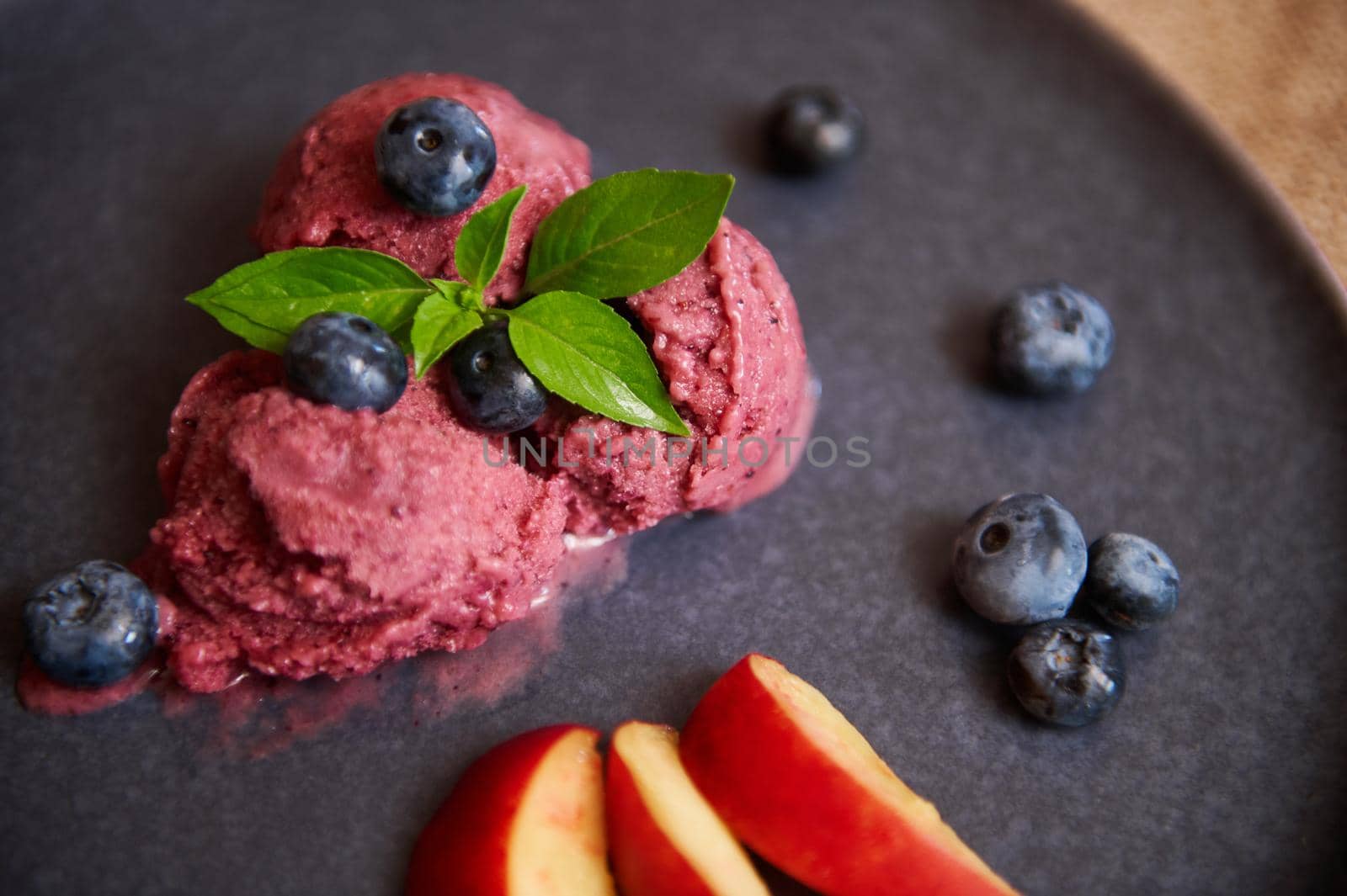 Still life of three purple frozen balls of organic blueberry sorbet, decorated with blueberries, lemon basil leaf and slices of ripe juicy peach. Healthy Live Food. Veganism Raw Food. Dieting concept