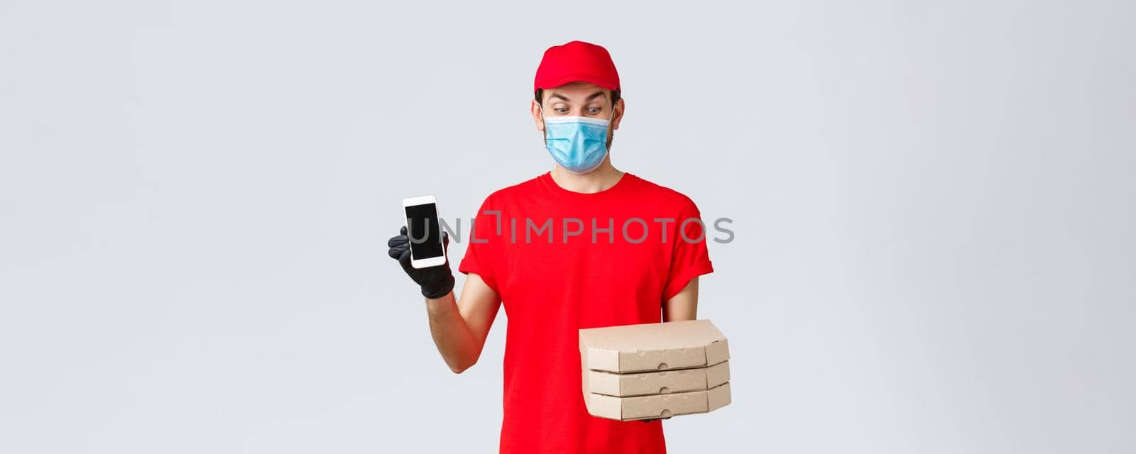 Food delivery, application, online grocery, contactless shopping and covid-19 concept. Excited courier in red uniform, looking at pizza boxes amused, showing smartphone screen app or bonus promo by Benzoix