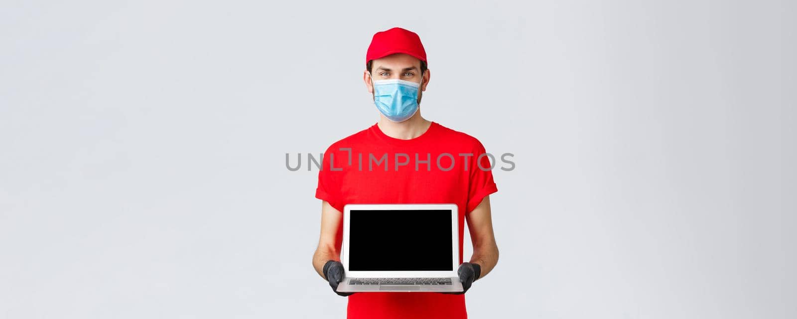 Customer support, covid-19 delivery packages, online orders processing concept. Smiling courier in red uniform, face mask and gloves, showing laptop screen webpage of company by Benzoix