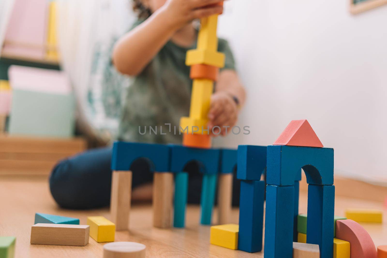 colorful wooden building blocks with a little girl unfocused in the background playing happy in the floor at home or kindergarten, educational toys for creative children