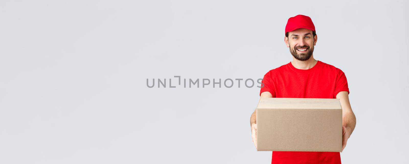 Order delivery, online shopping and package shipping concept. Friendly smiling bearded courier in red uniform t-shirt and cap, giving out package for customers, handing box to client.