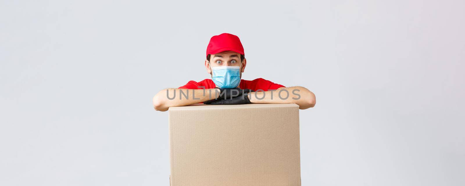 Packages and parcels delivery, covid-19 quarantine and transfer orders. Worried and confused courier in red uniform, gloves and face mask, lean on order box and look surprised camera.