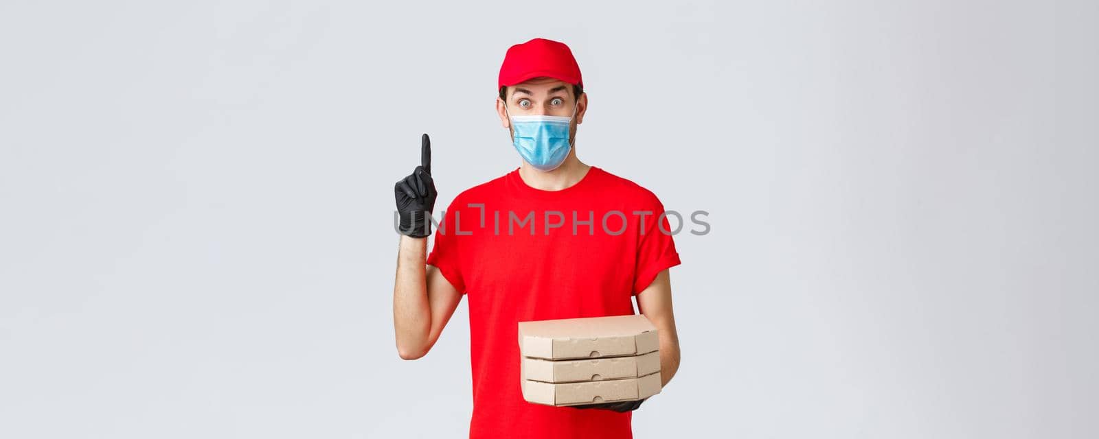 Food delivery, application, online grocery, contactless shopping and covid-19 concept. Excited delivery guy in red uniform, gloves and face mask, have suggestion, hold pizza and raise finger.