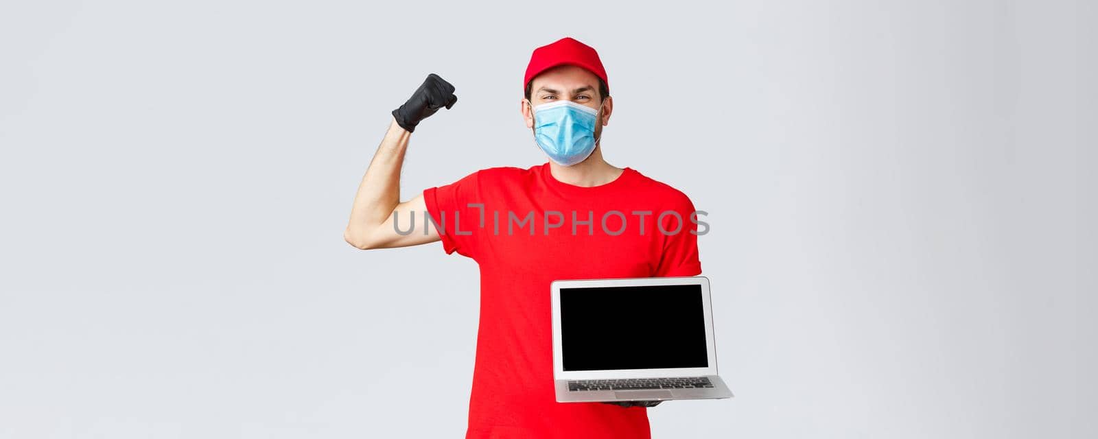 Customer support, covid-19 delivery packages, online orders processing concept. Rejoicing happy courier lift hand in yes, celebration, showing laptop screen, wear face mask and gloves.