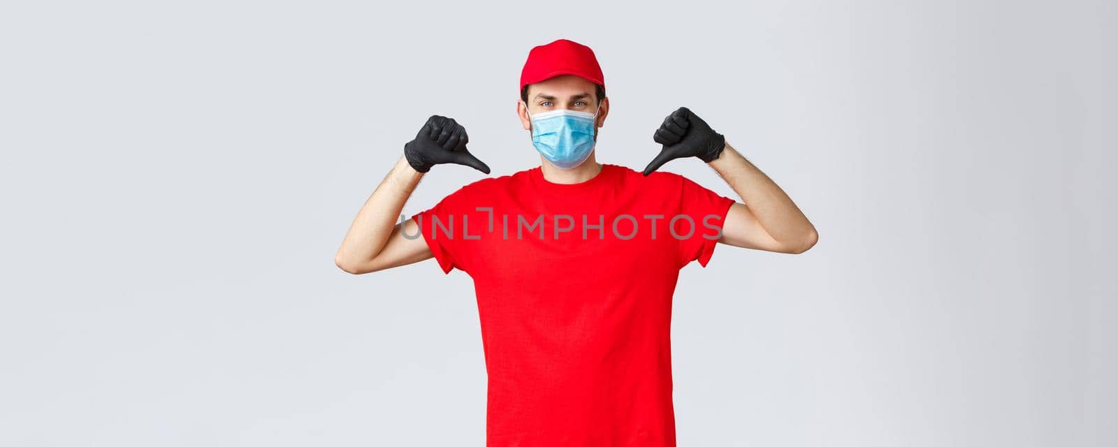Groceries and packages delivery, covid-19, quarantine and shopping concept. Confident serious courier in red uniform, face mask and gloves assure delivery service quality, pointing at himself.