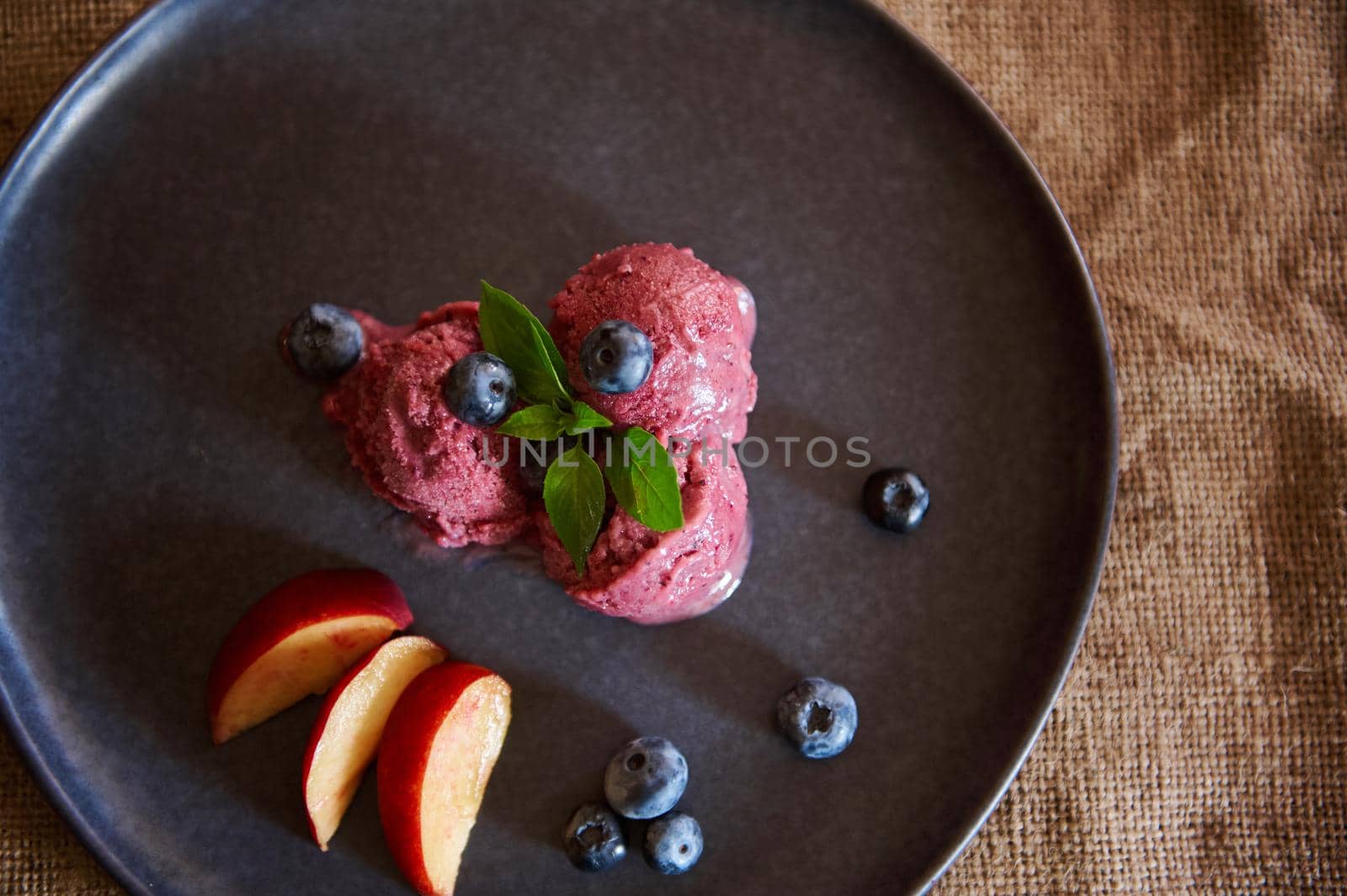 Flat lay. Healthy, sweet, raw vegan homemade dessert for refreshment on hot summer days. Refreshing blueberry sorbet, ice cream with slices of ripe juicy peach, blueberries and mint leaves. Copy space