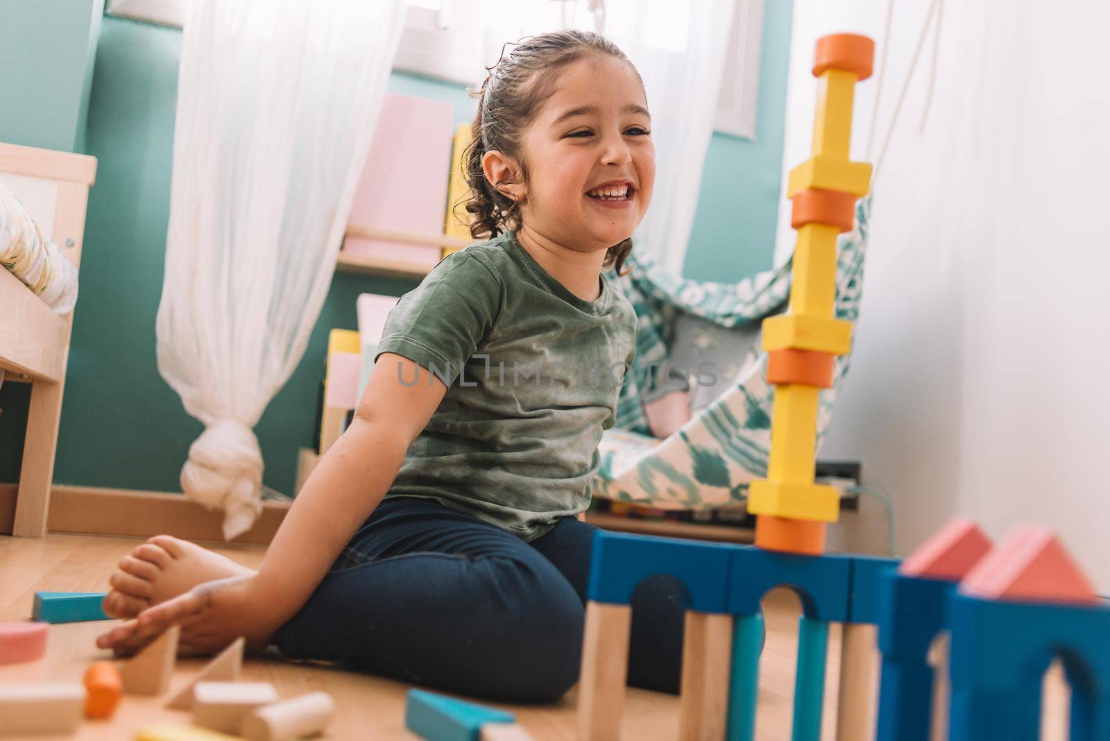 funny little girl smiling while playing happy in the floor with colorful wooden building block toys at home or kindergarten, educational toys for creative children