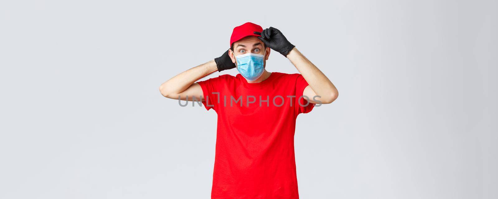Groceries and packages delivery, covid-19, shopping concept. Excited surprised delivery man in red uniform, fix cap on head and staring interested camera, courier on duty during coronavirus by Benzoix