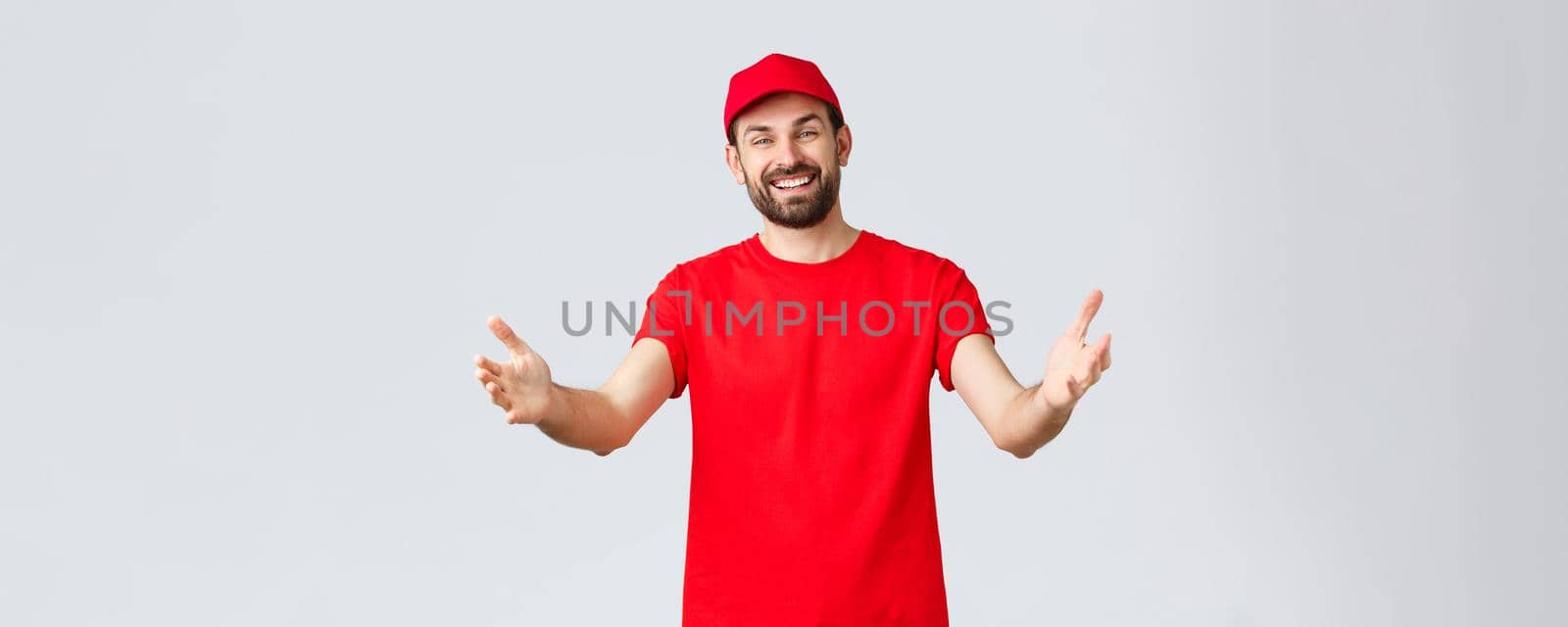 Online shopping, delivery during quarantine and takeaway concept. Friendly pleasant courier in red t-shirt and cap, company uniform, reaching hands towards client or order, taking package by Benzoix