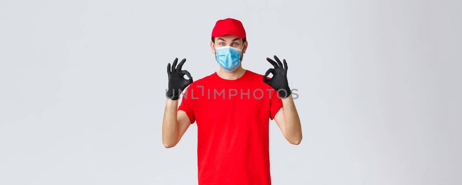 Covid-19, self-quarantine, online shopping and shipping concept. Excited delivery guy in red cap, t-shirt and face mask working coronavirus outbreak, show okay sign, guarantee safe courier service.