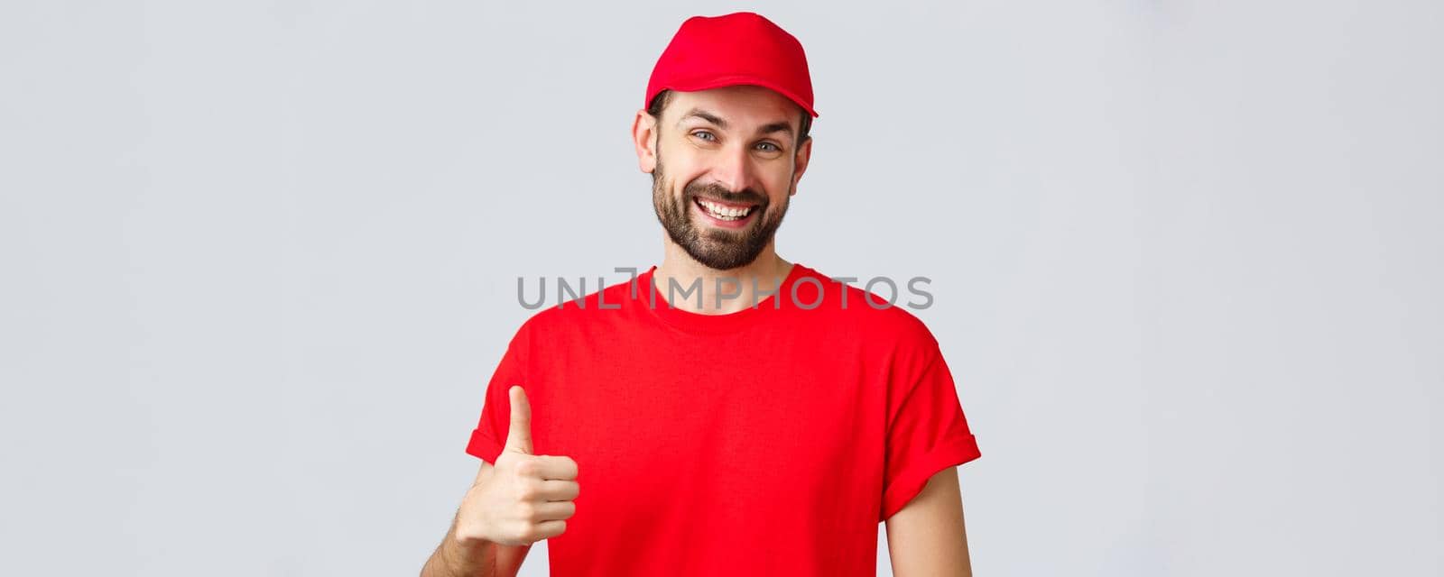 Online shopping, delivery during quarantine and takeaway concept. Friendly, cheerful courier in red cap and t-shirt uniform, encourage make internet orders, thumb-up in approval or recommendation by Benzoix