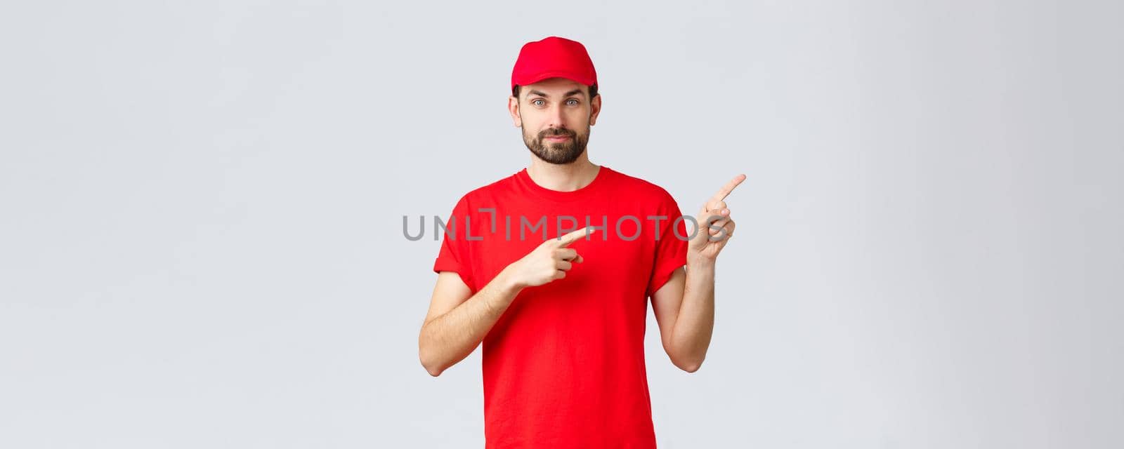Online shopping, delivery during quarantine and takeaway concept. Confident bearded courier in red uniform cap and t-shirt, smiling camera, give direction, pointing finger right, inform clients.