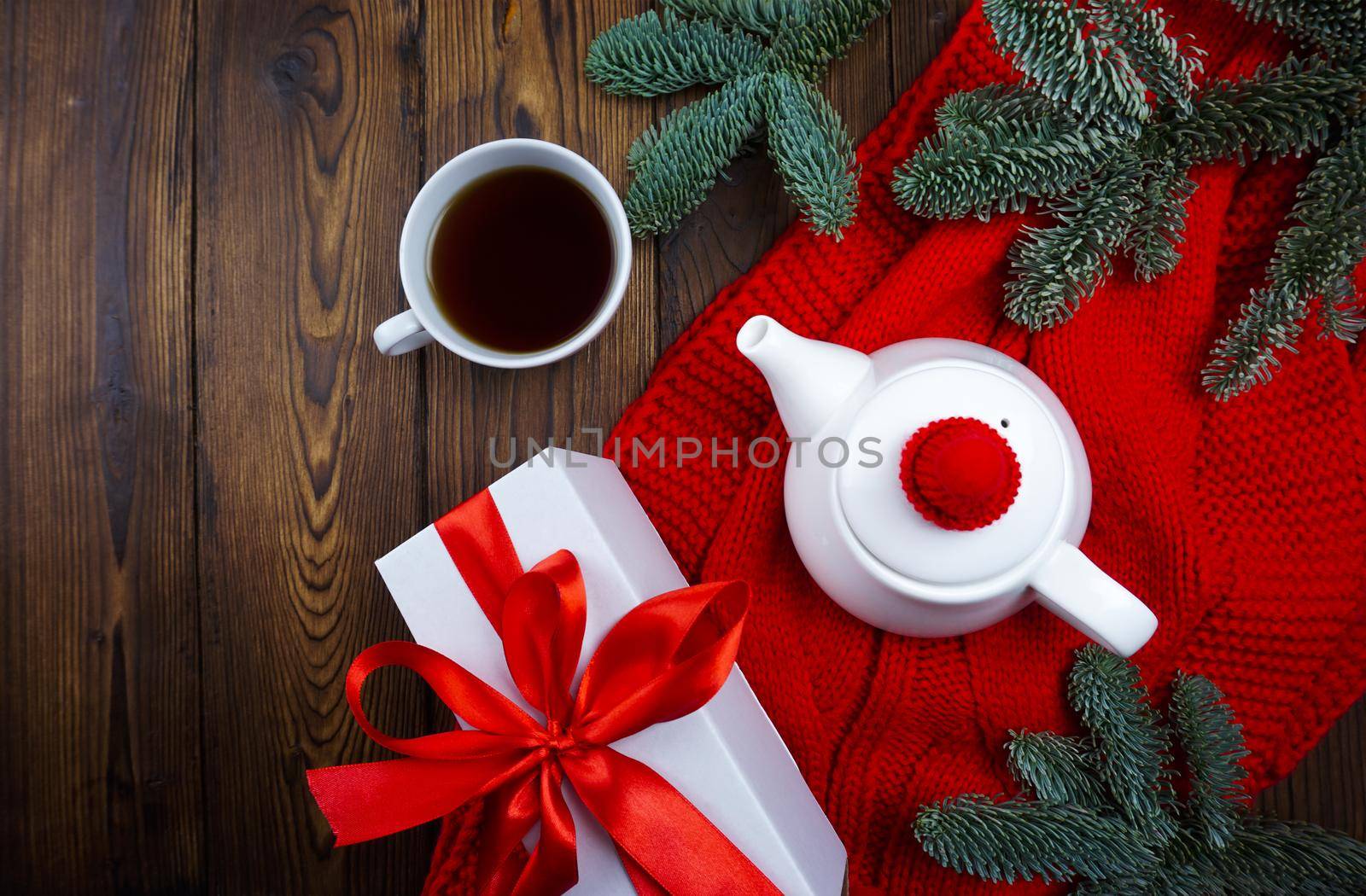 Tea is poured in a white teapot and glass, next to it lies a red plaid, Christmas balls and coniferous branches by Spirina