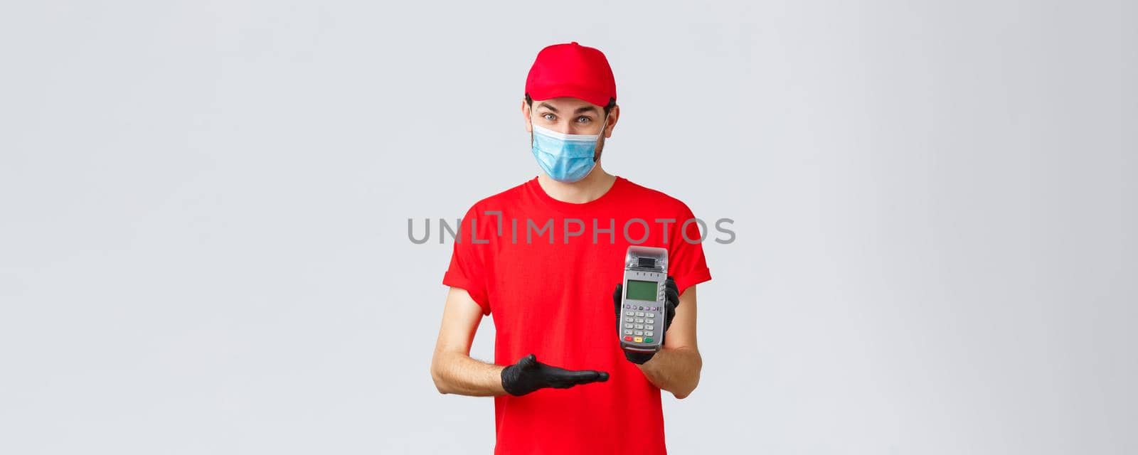 Contactless delivery, payment and online shopping during covid-19, self-quarantine. Pleasant courier in red uniform, face mask and gloves, asking use POS terminal to pay order by Benzoix