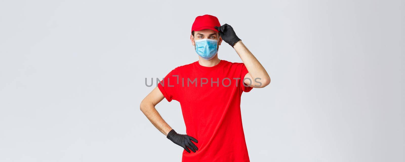 Covid-19, self-quarantine, online shopping and shipping concept. Delivery guy red uniform, touching cap as saluting customer, working in coronavirus outbreak, wear medical mask and protective gloves.