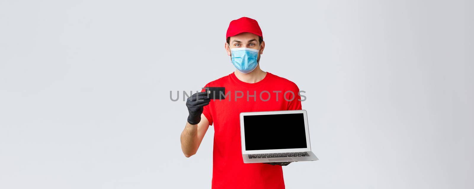Customer support, covid-19 delivery packages, online orders processing concept. Smiling courier in red uniform cap and t-shirt, medical face mask, credit card paying for orders and show laptop.