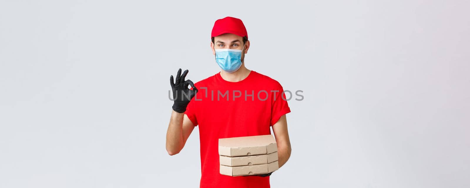 Food delivery, application, online grocery, contactless shopping and covid-19 concept. Courier guarantee quality of pizza, holding boxes, showing okay sign in recommendation or approval, wear mask by Benzoix