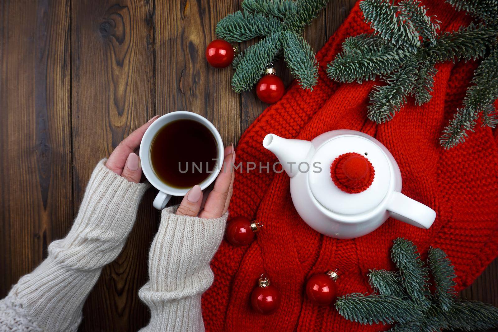 Tea is poured in a white teapot and glass, next to it lies a red plaid, Christmas balls and coniferous branches by Spirina